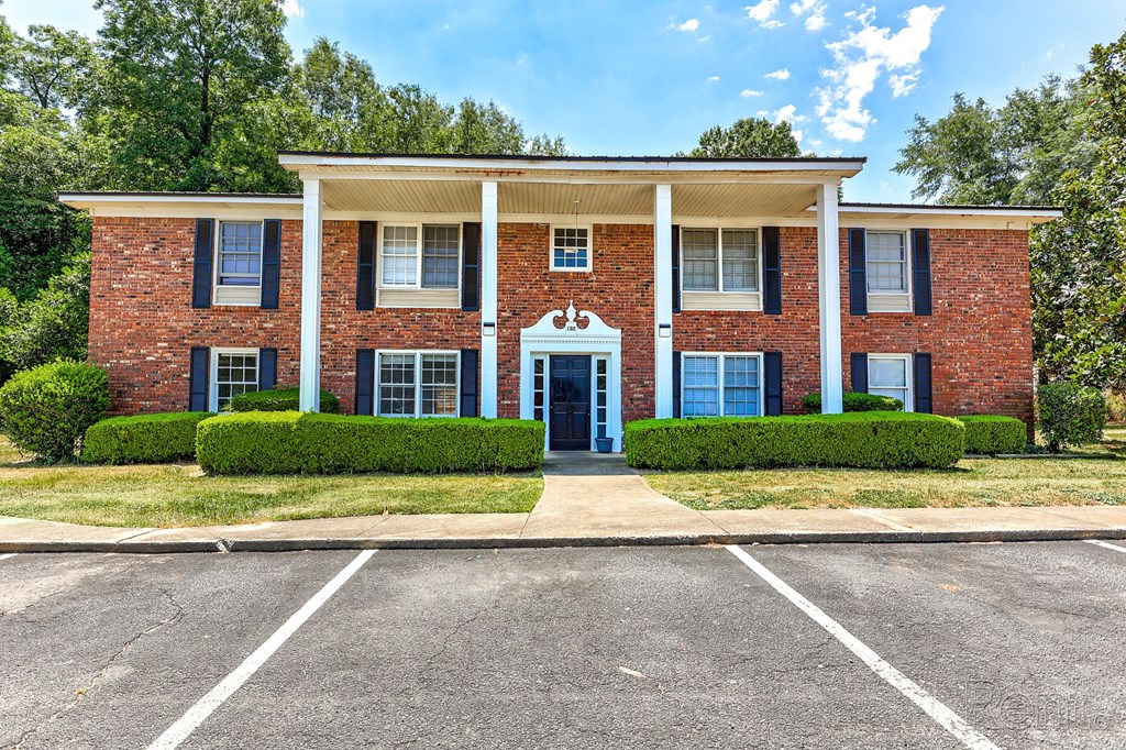 A red brick residential building with columns and a parking lot in front.