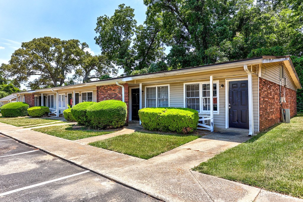 A row of residential units with green bushes and a sidewalk in front.