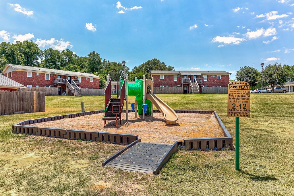 A playground with a green slide and residential buildings in the background.