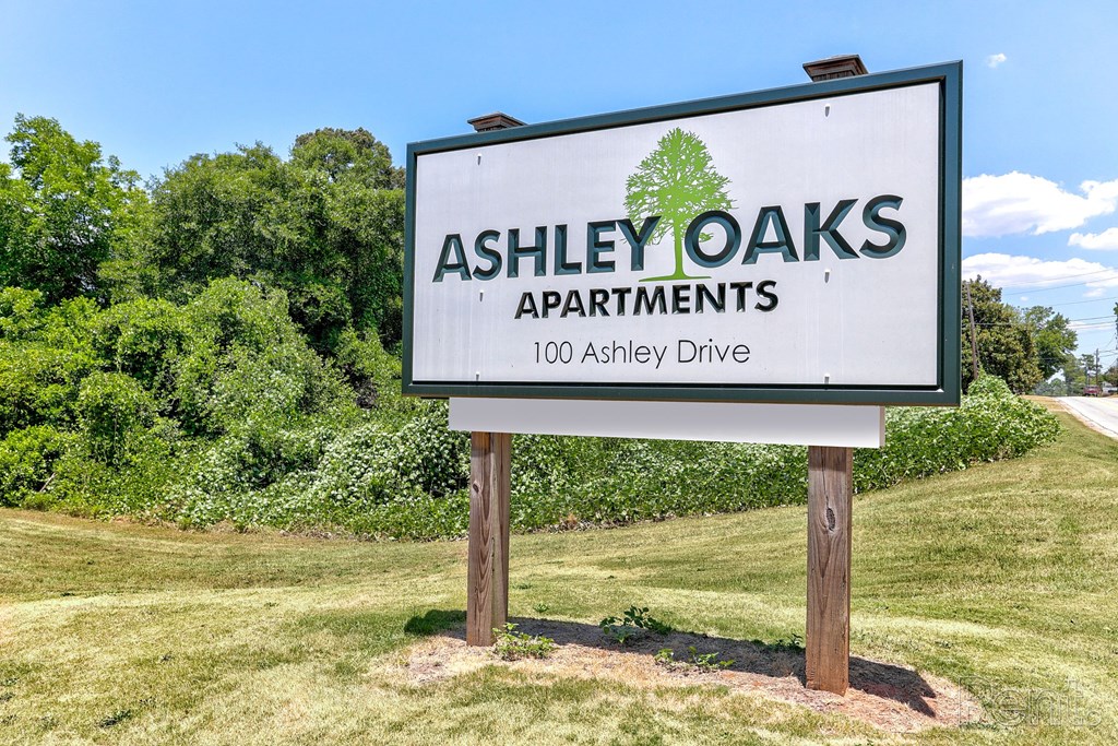 A sign for Ashley Oaks Apartments with grass and trees surrounding it.