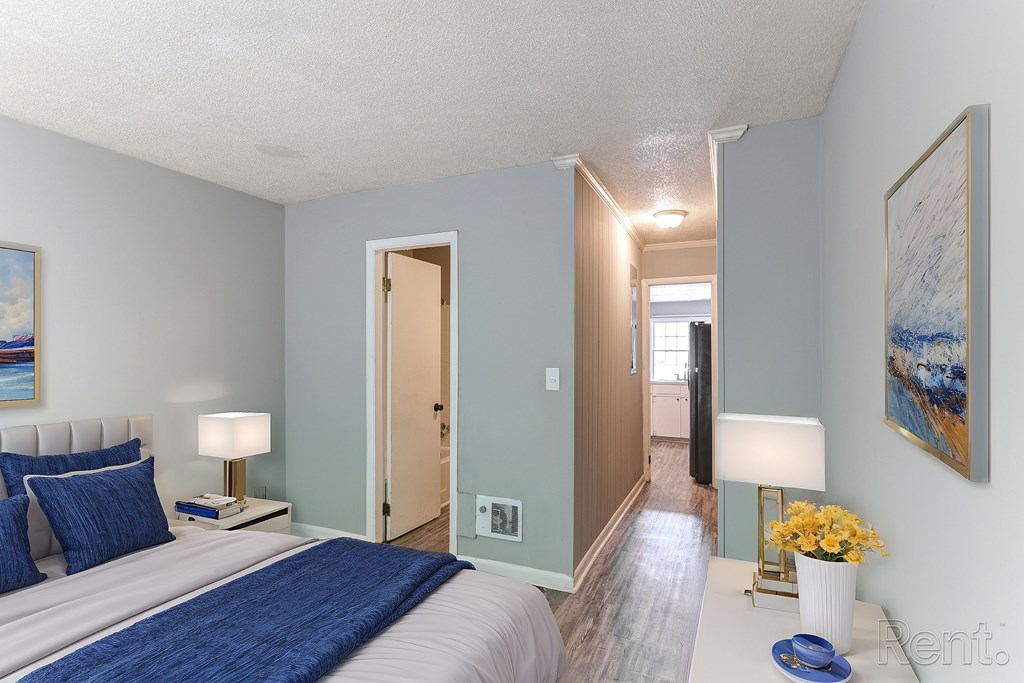 A bedroom with a bed, a lamp on a nightstand, and a painting on the wall.