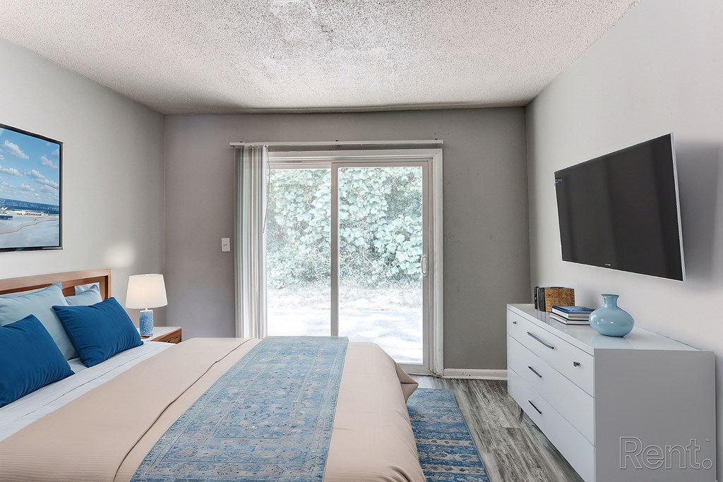 A bedroom with a bed, flat screen TV, and a view of the outdoors through a sliding glass door.