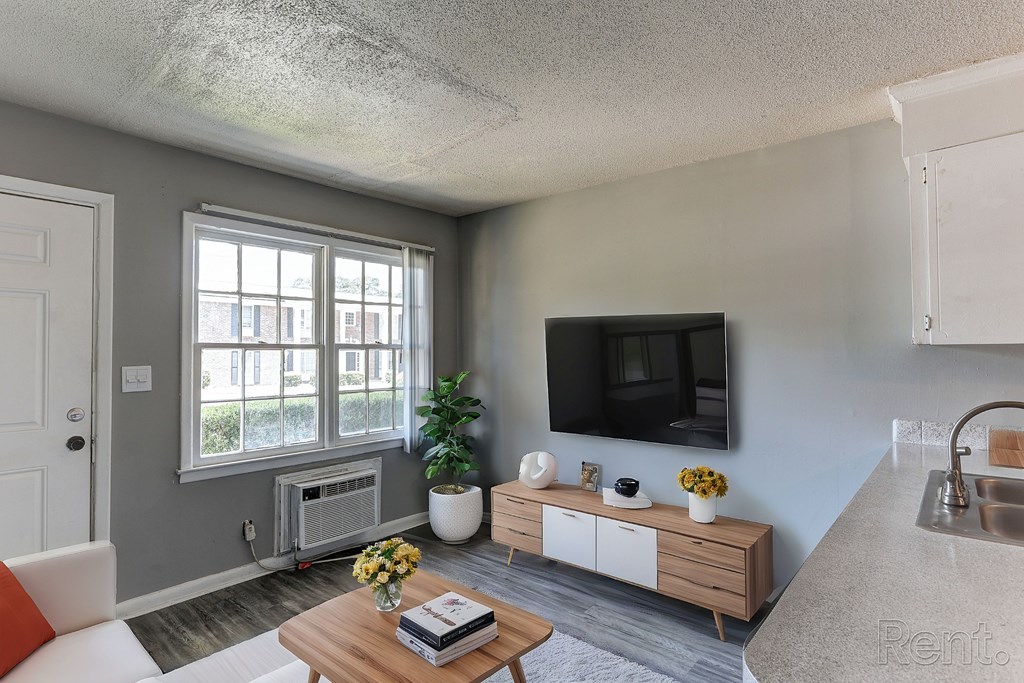 A living room with a white couch, a wooden coffee table, a flat screen TV, and a window with a view of buildings outside.
