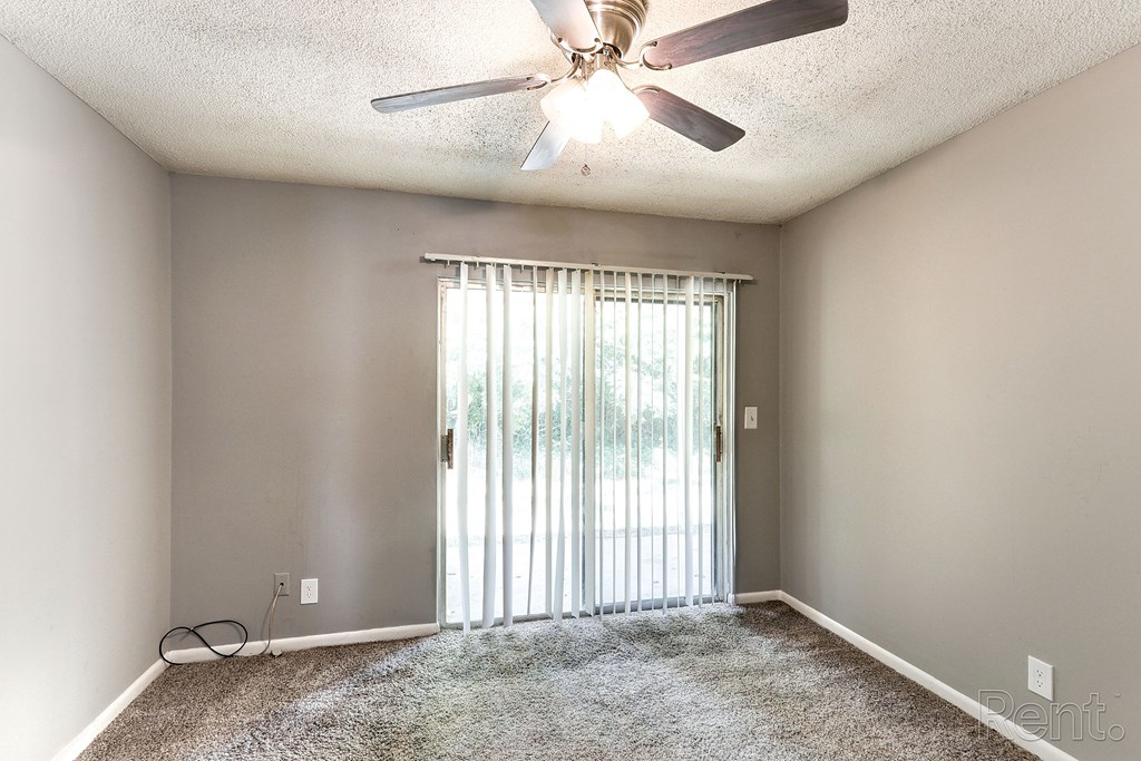 A room with a ceiling fan, a carpeted floor, and a sliding glass door leading outside.