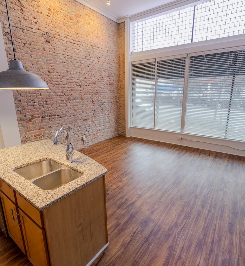 A kitchen with a brick wall and wooden floors.