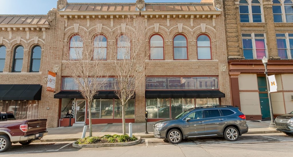 A tree in front of a building with a car parked in front of it.