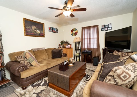 A living room with a brown couch, a coffee table, and a ceiling fan.