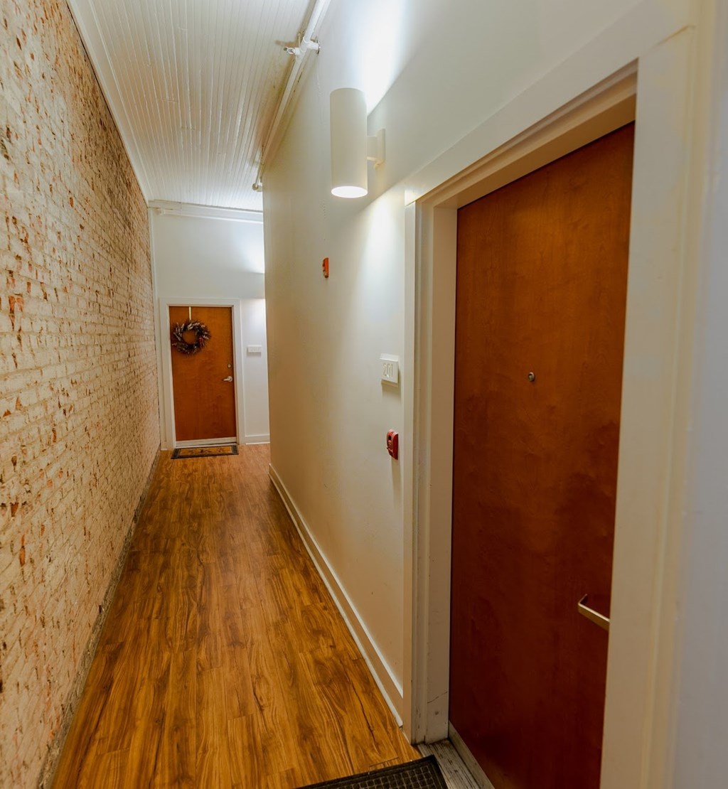 A hallway with a brick wall on the left and a wooden door on the right.