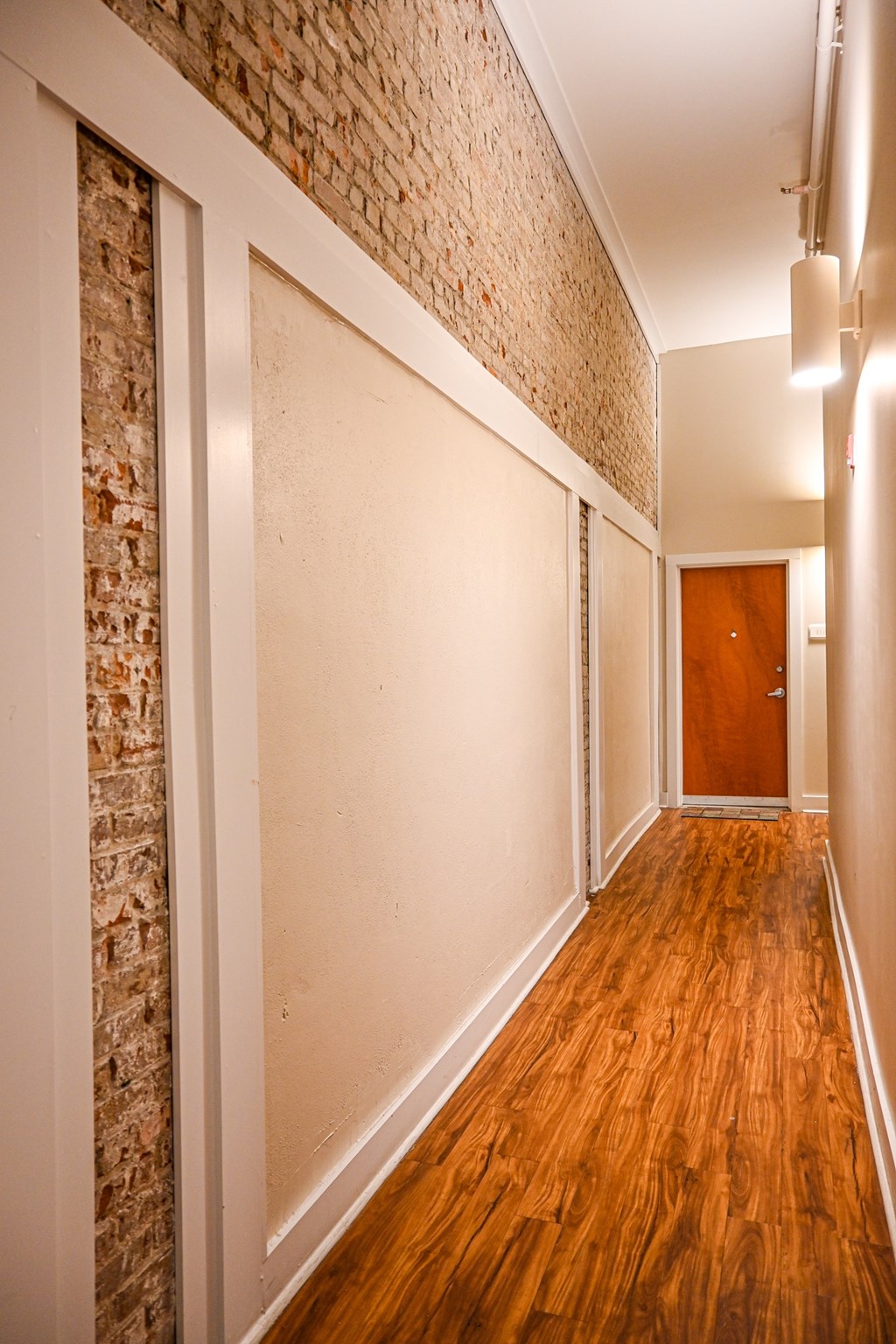 A long hallway with a brick wall on the left and a wooden door on the right.