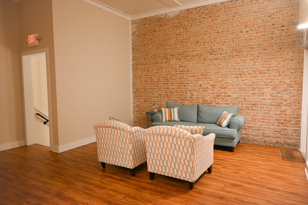 Two chairs and a couch are in a room with a brick wall.