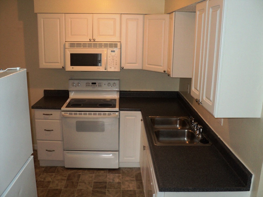 A kitchen with white cabinets and black countertops.