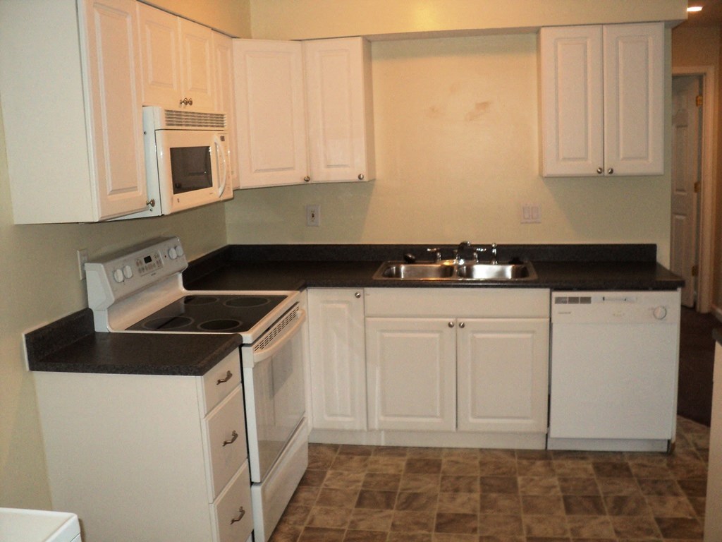 A kitchen with white cabinets and black countertops.