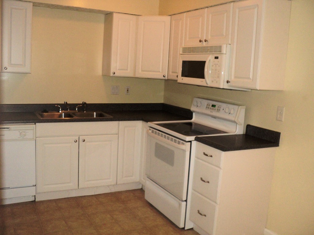 A white kitchen with black countertops and white appliances.