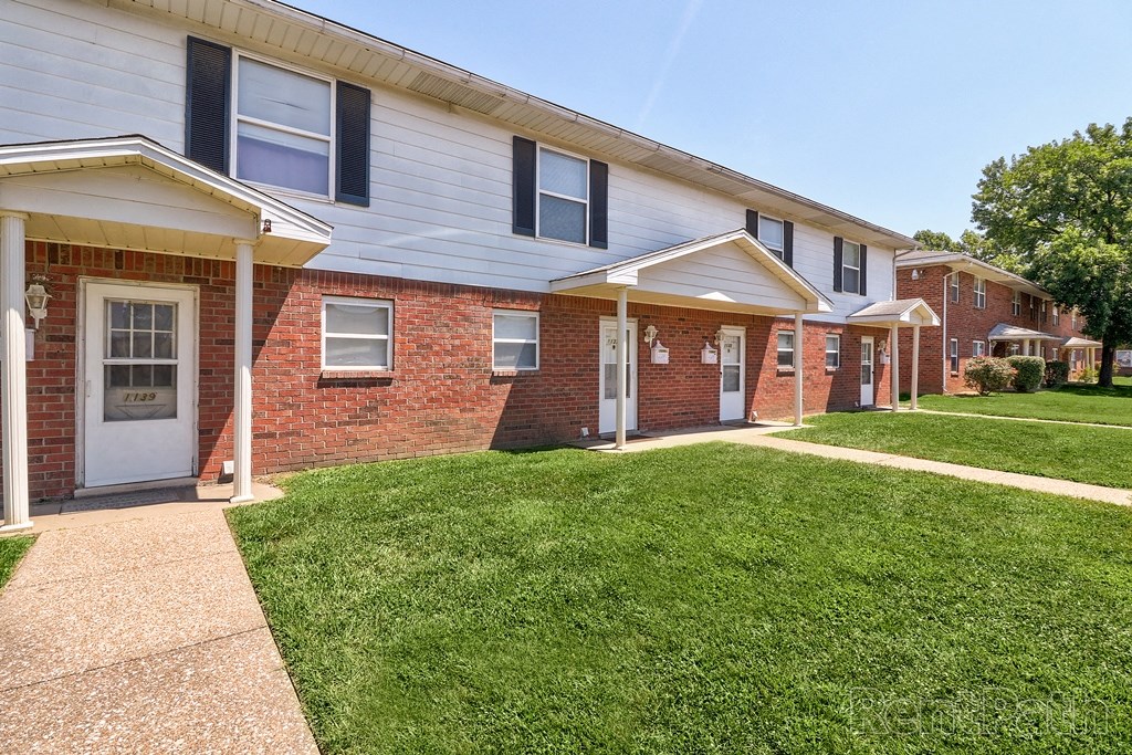 a brick apartment building with a lawn and a sidewalk