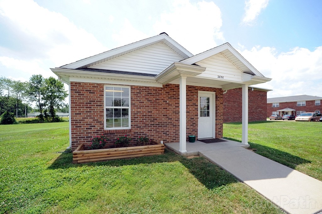 a small brick house with a porch and a lawn