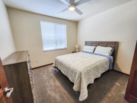 A bedroom with a bed, a ceiling fan, and a window.