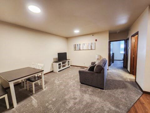 A living room with a grey couch, a table, and a television.