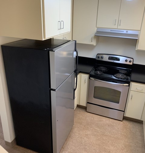 A black refrigerator stands next to a silver oven in a kitchen.