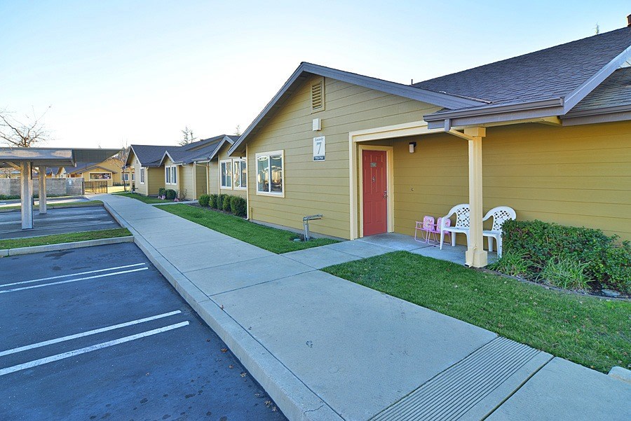 A yellow house with a red door is in the foreground of a street with other houses in the background.