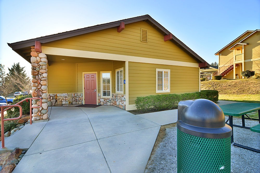 A yellow house with a red door and a green trash can in front.