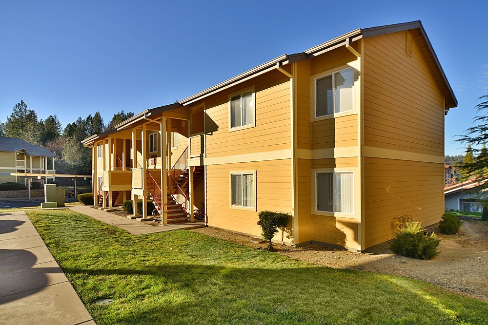 A yellow house with a brown roof and a green lawn in front.