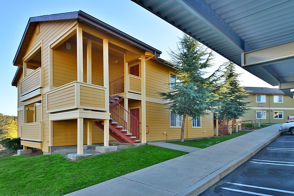 A yellow house with a red staircase and a tree in front.