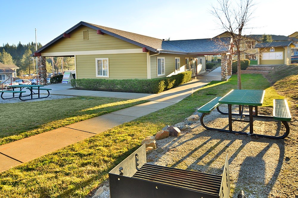 A park with a picnic table and a bench in front of a building.