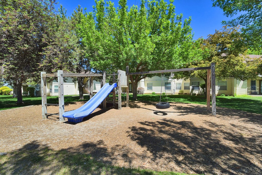 A playground with a blue slide and a wooden swing set.
