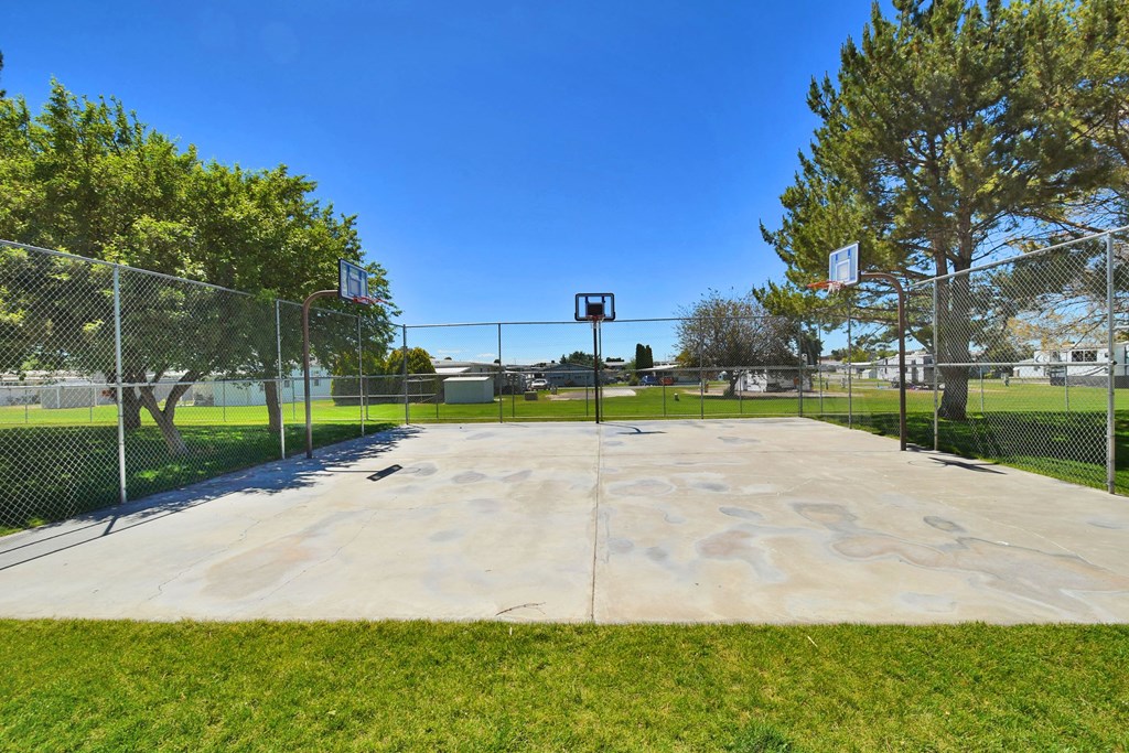 A basketball court surrounded by a fence with a basketball hoop in the middle.