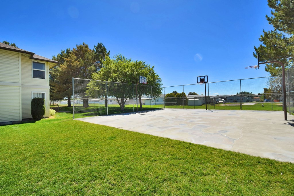 A basketball court surrounded by a fence and a grassy area in front.