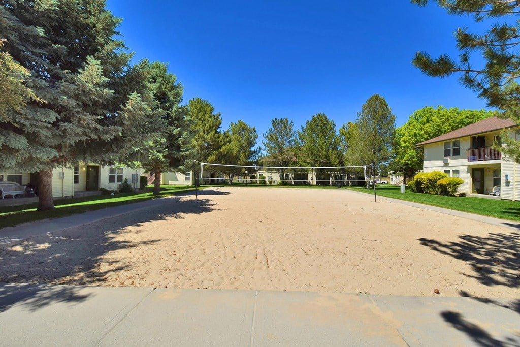 A sandy area in front of a row of houses with trees on the side.