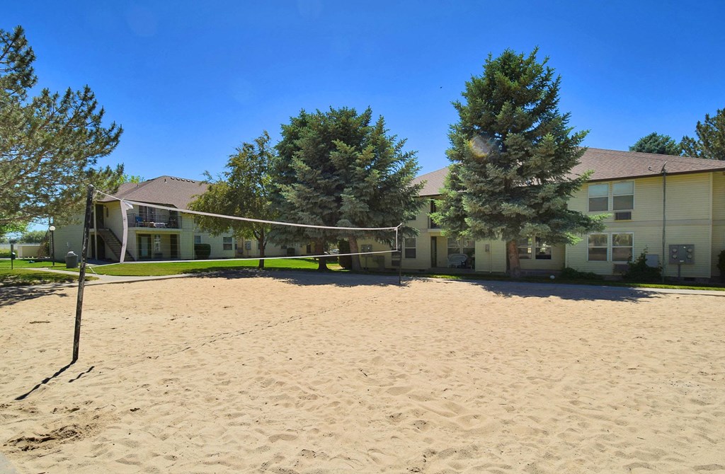 A sandy volleyball court in front of a building with trees in the background.