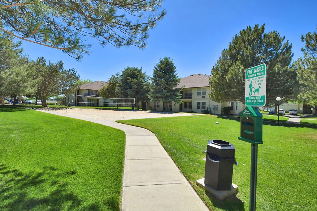 A green sign in a park with a trash can next to it.