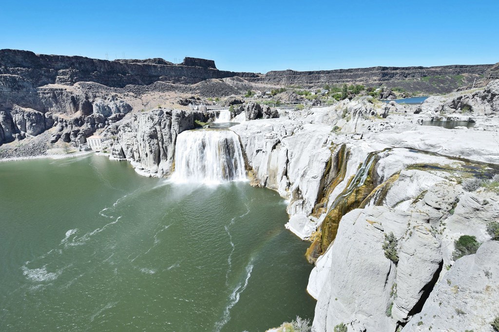 A waterfall cascades into a green lake surrounded by rocky cliffs.