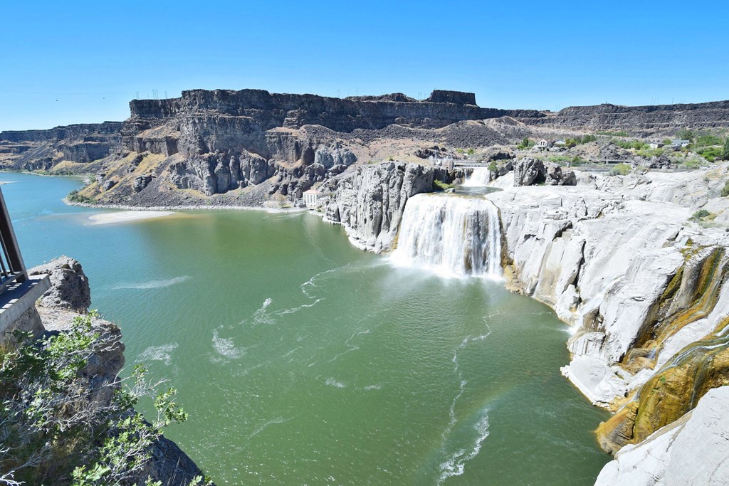 A large waterfall cascades into a green lake surrounded by rocky cliffs.