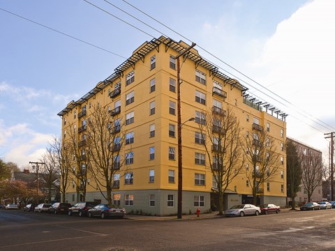 A yellow building with a green base and a parking lot in front.