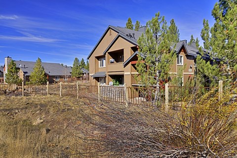 A house with a brown roof and a grey garage door is surrounded by a fence and trees.