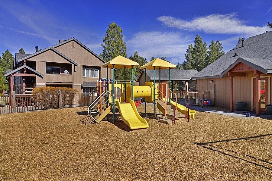 A playground with a yellow slide and a brown sandy ground.