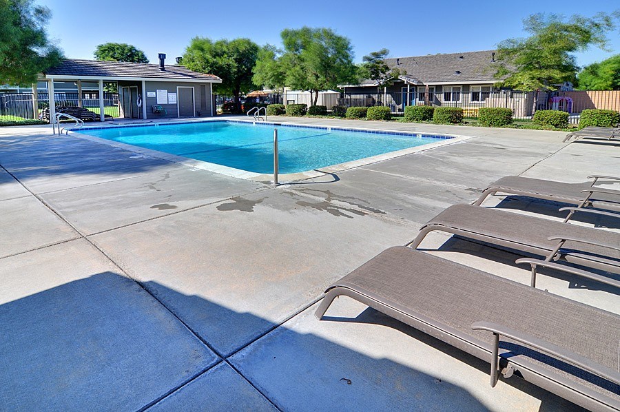 A pool with sun loungers and a pavilion in the background.