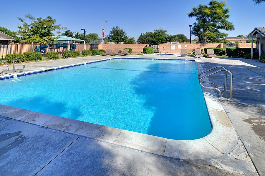 A large blue swimming pool with a concrete edge and a metal ladder on the right side.