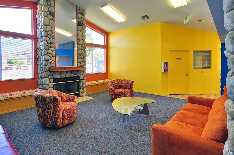A yellow room with a stone fireplace and a red chair.