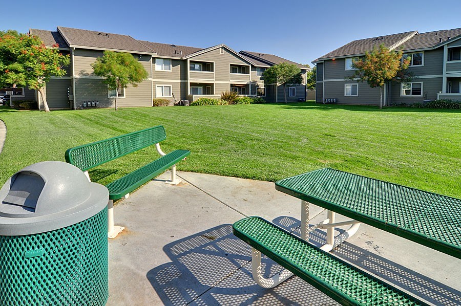A green trash can sits next to a green picnic table in a grassy area.