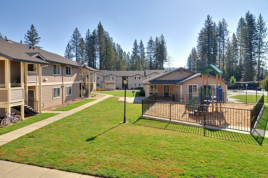 A playground with a swing set and a fence is in the foreground of a residential area with houses and trees in the background.