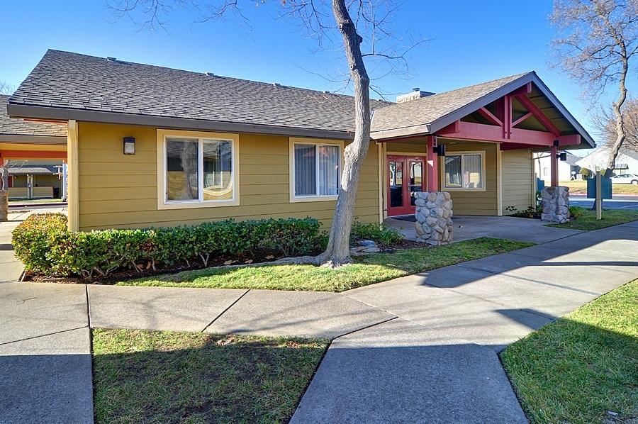 A yellow house with a red trim and a stone pillar in front.