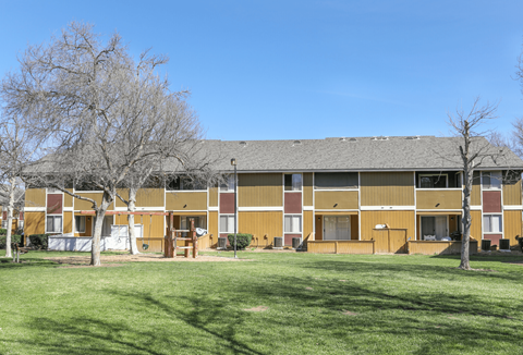 A building with a brown and tan exterior is surrounded by a green lawn.