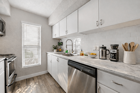 A kitchen with a stainless steel dishwasher and white cabinets.