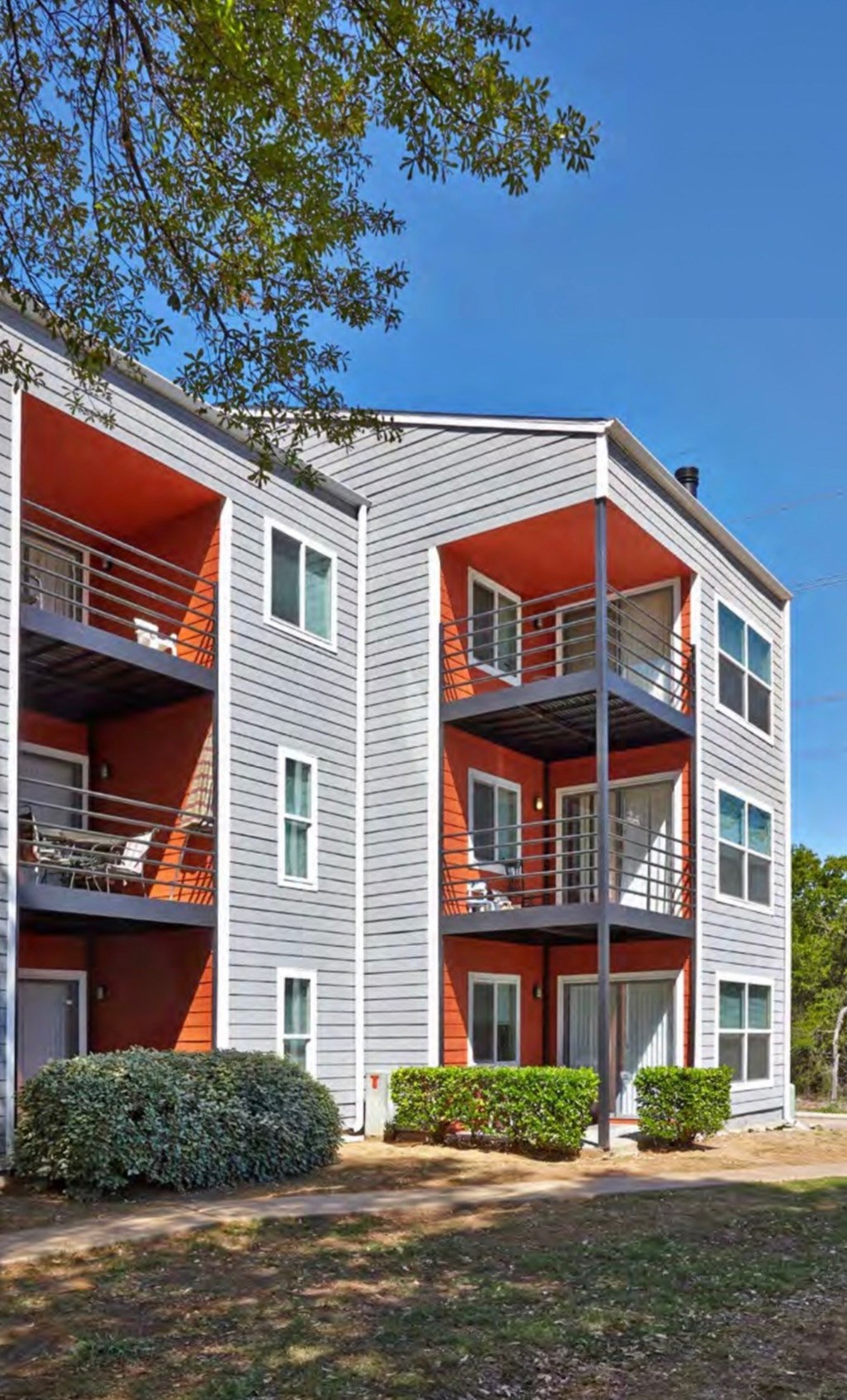 A modern two-story apartment building with red accents on the balconies and doors at Infinity on the Landing Apartments, Texas