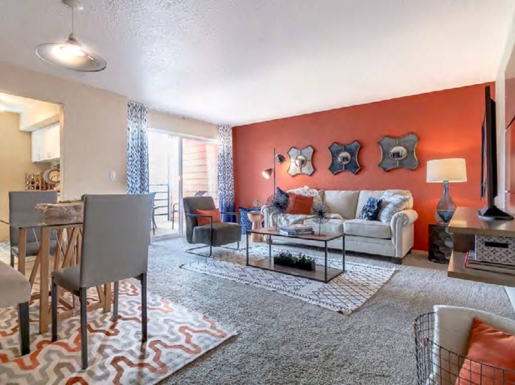 A living room with a grey sofa, a grey armchair, a glass coffee table and a rug at Infinity on the Landing Apartments, Euless, TX