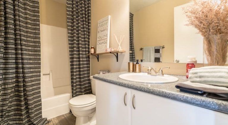 A bathroom with a toilet, sink, and a mirror at Infinity on the Landing Apartments, Euless, TX