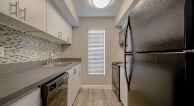 A kitchen with a black refrigerator, white cabinets, and a tiled backsplash at Infinity on the Landing Apartments, Euless